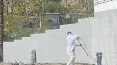 Painter spraying a block wall white in protective suit